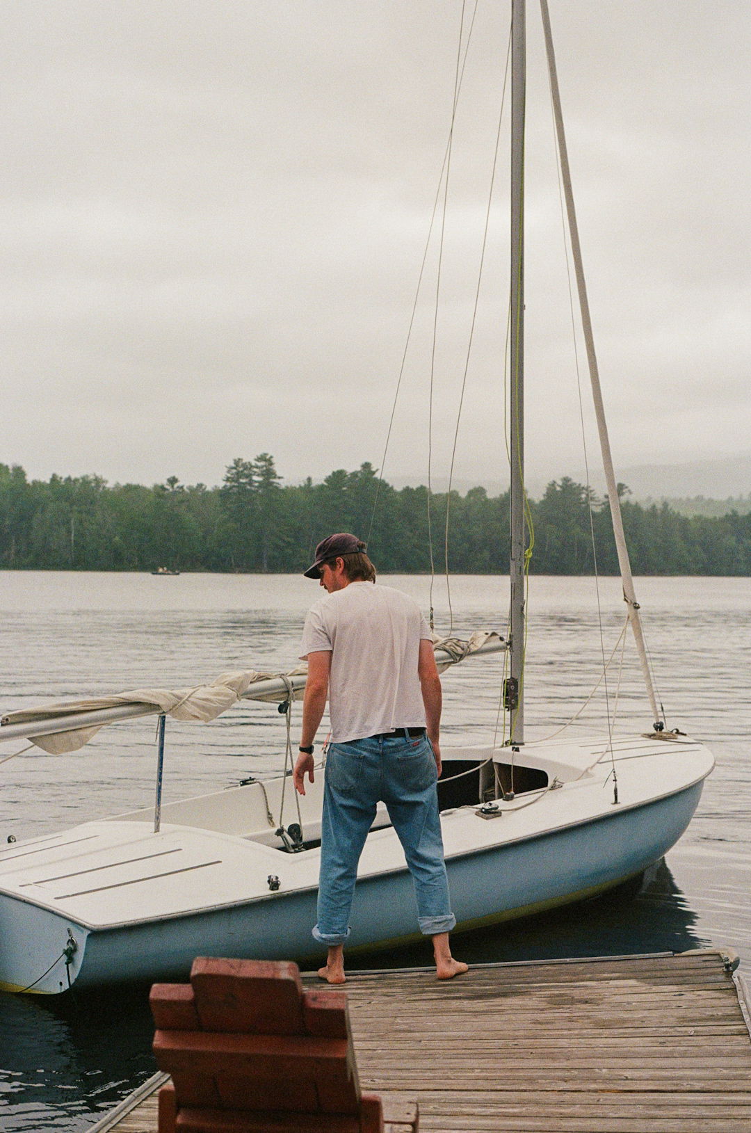 Man standing next to his sailboat at the dock.